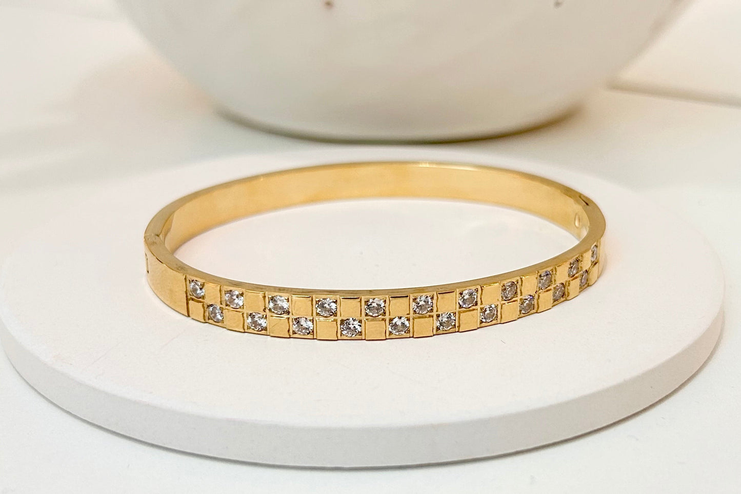 
                  
                    Elisia Gold Square Crystal Bangle displayed on a white stand
                  
                