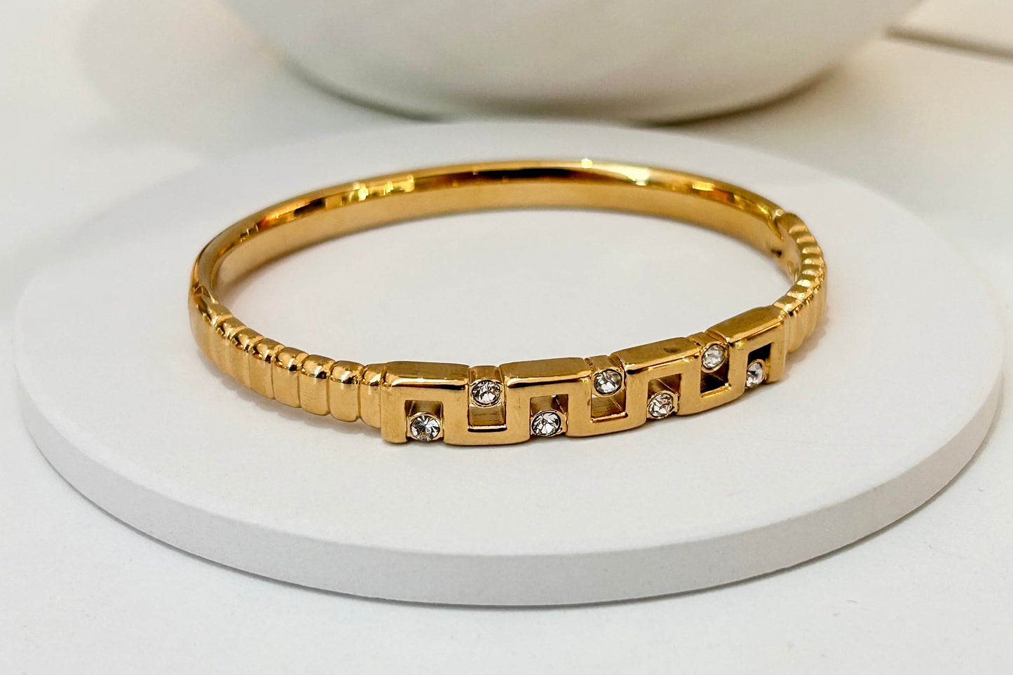 
                  
                    Marcella Gold Geometric Crystal Bangle displayed on a white stand
                  
                