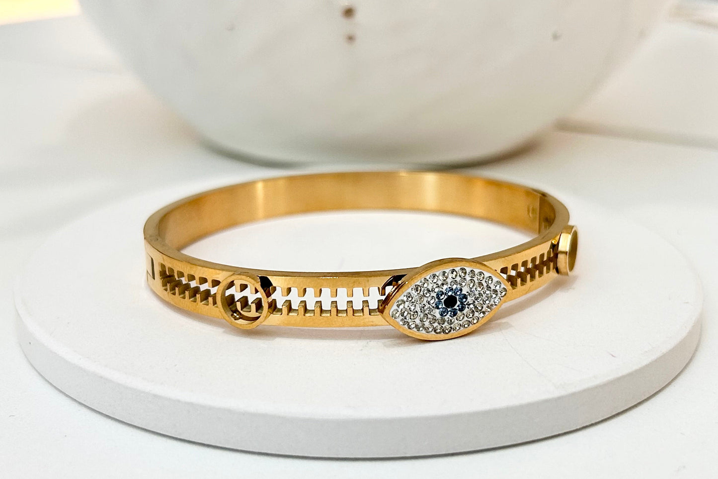 
                  
                    Nazari Evil Eye Gold Bangle displayed on a white stand
                  
                
