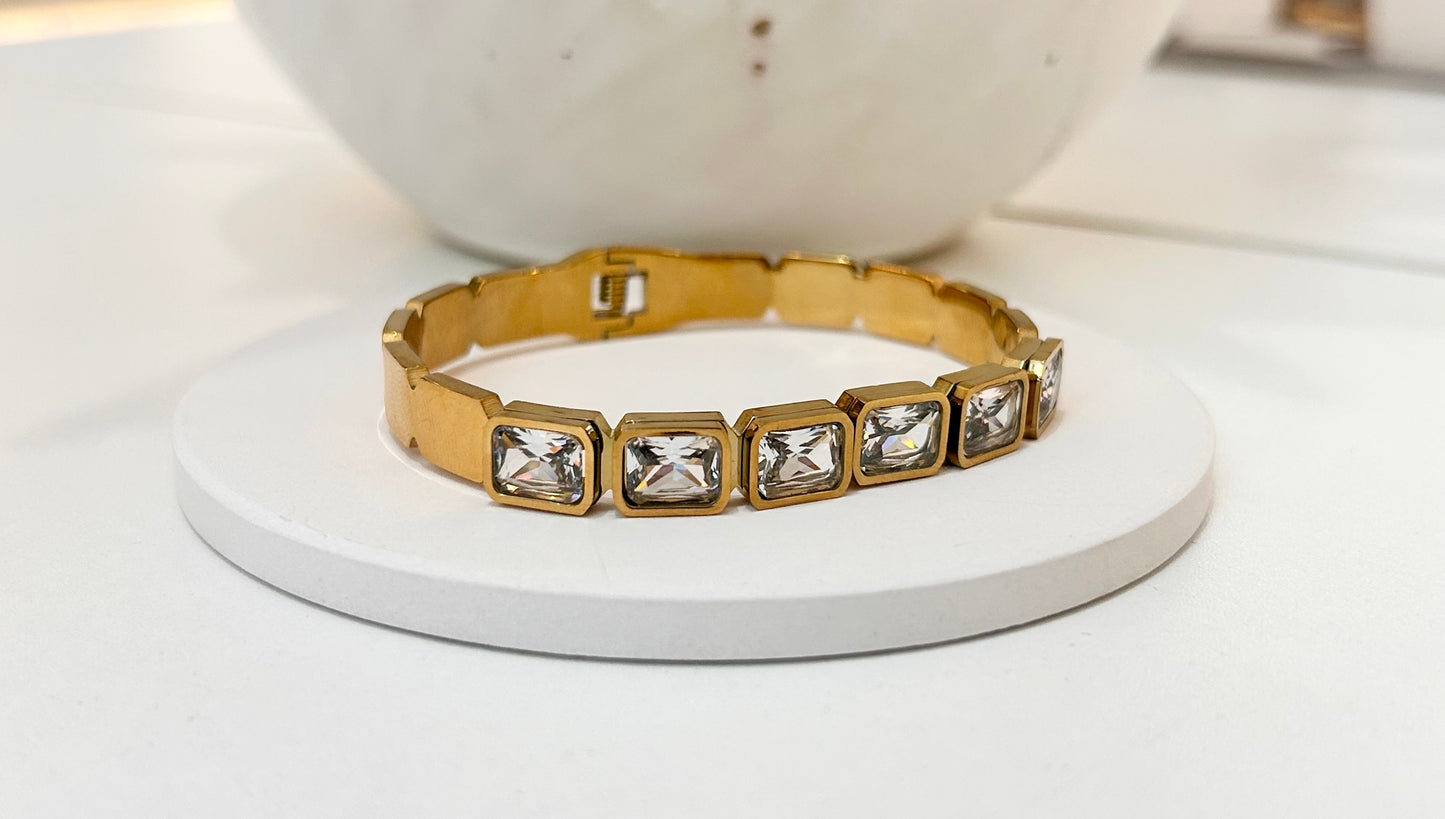 
                  
                    Lorienne Gold Emerald-Cut Crystal Bangle displayed on a white stand
                  
                