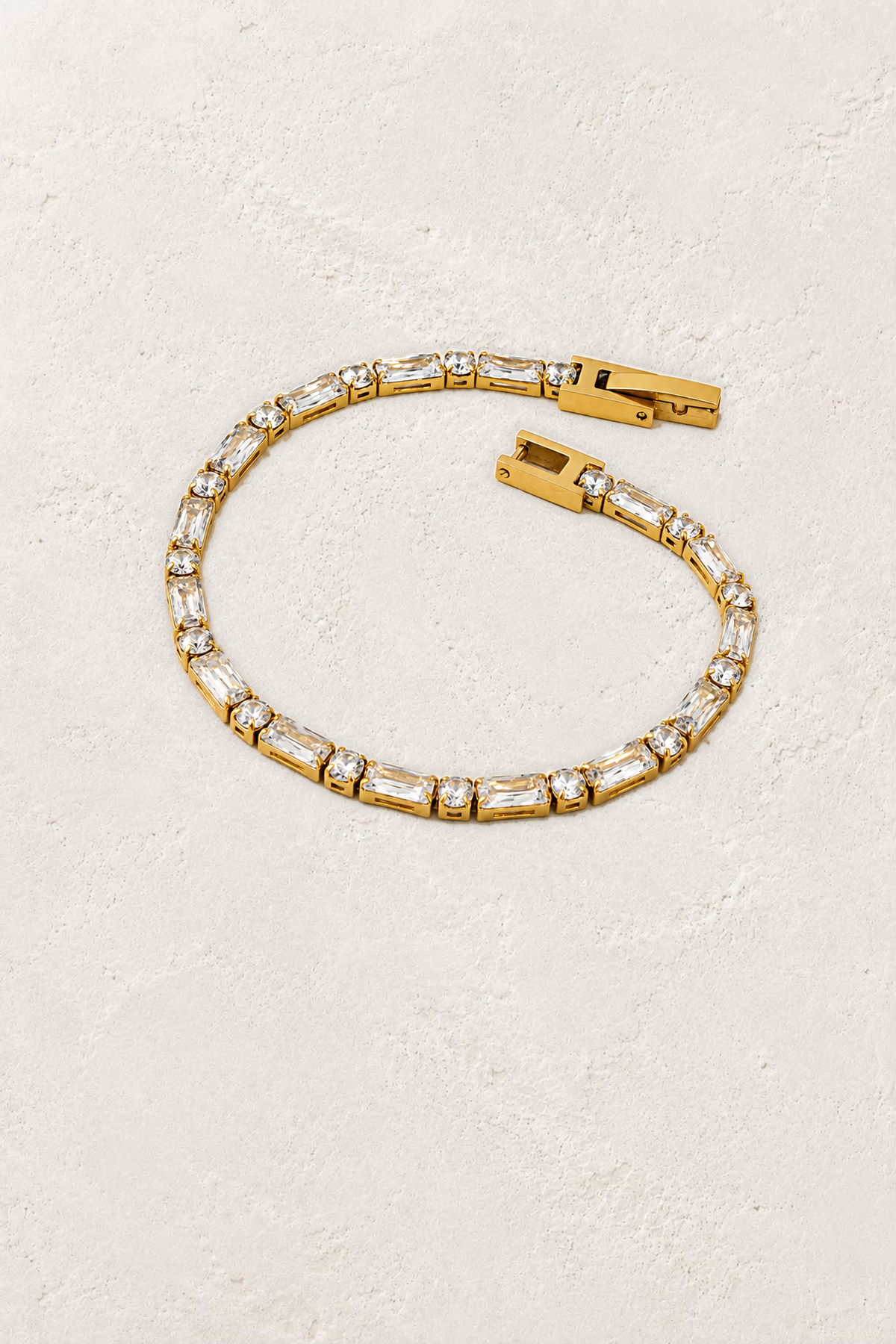 Avelisse Emerald & Round Crystal Gold Tennis Bracelet on the reference plaster background