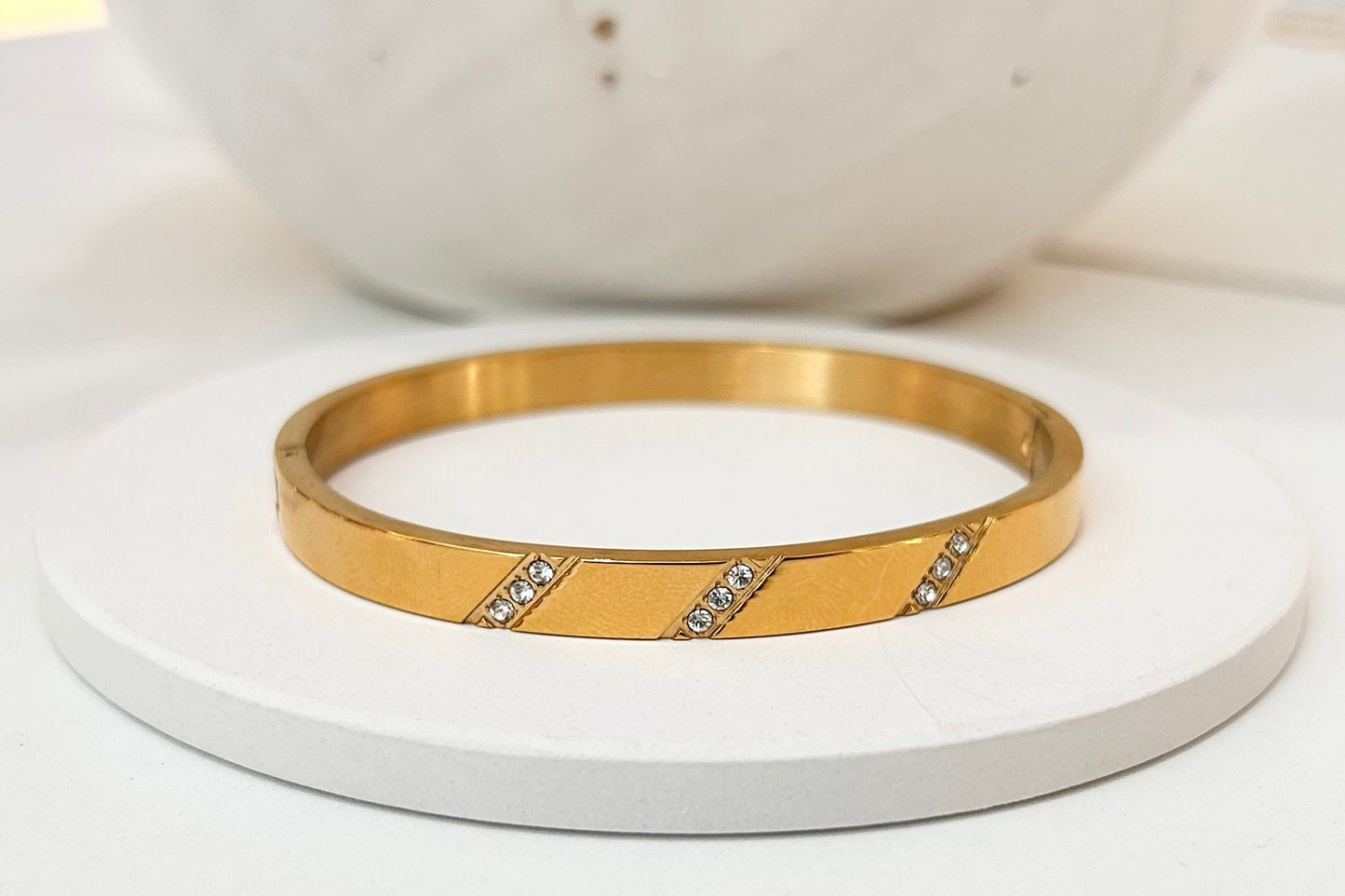 
                  
                    Lucienne Brushed Gold Diagonal Crystal Bangle displayed on a white stand
                  
                