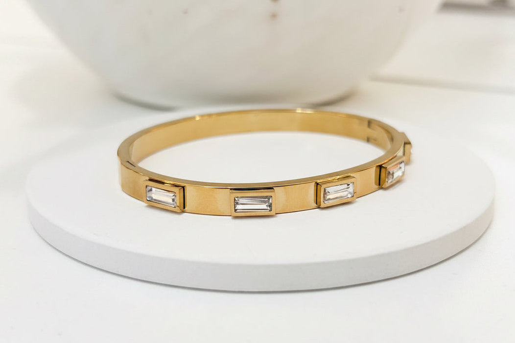 
                  
                    Emerelle Clear Crystal Gold Bangle displayed on a white stand
                  
                