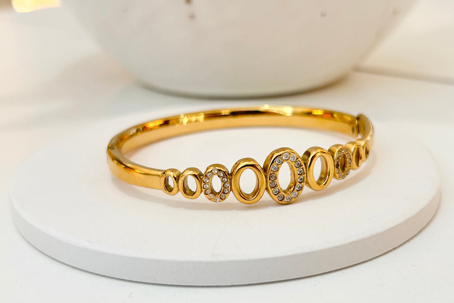
                  
                    Amoura Open Oval Gold Crystal Bangle displayed on a white stand
                  
                
