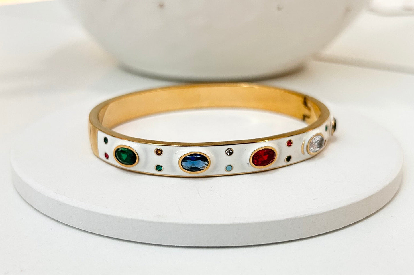 
                  
                    Fiorella White Enamel Multi-Crystal Gold Bangle displayed on a white stand
                  
                