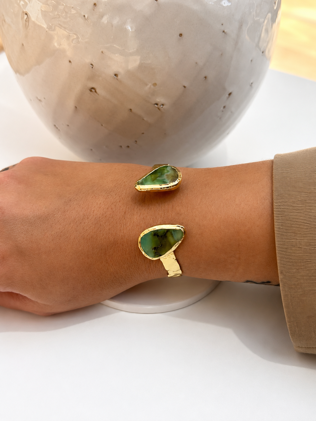 
                  
                    Gold bracelet with green chrysoprase stones on a wrist against a neutral background
                  
                