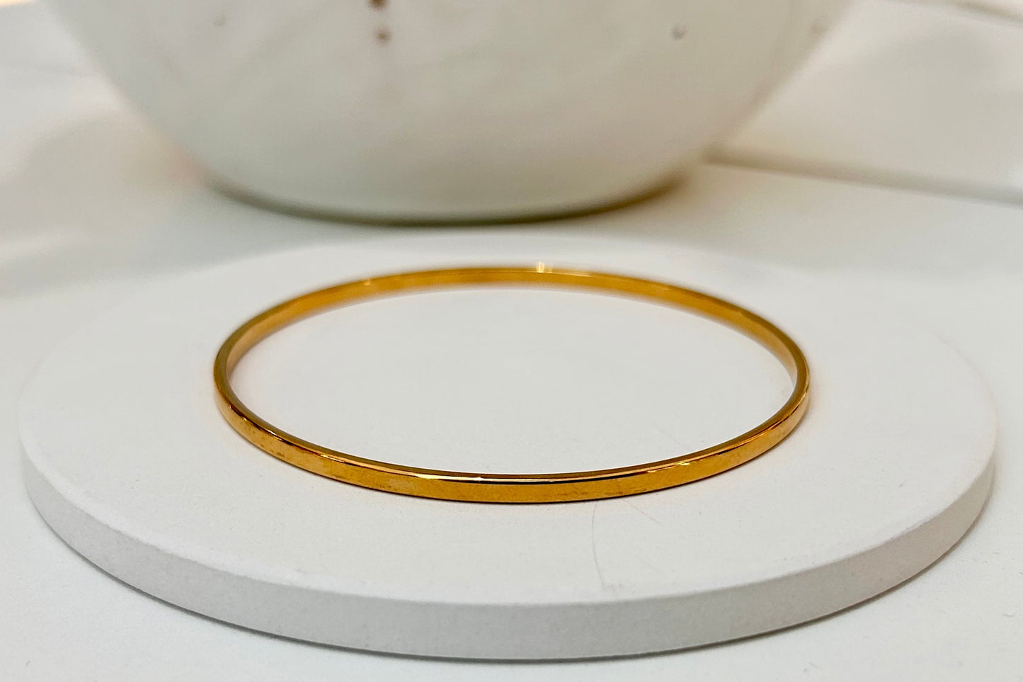 
                  
                    Serenelle Slim Polished Gold Bangle displayed on a white stand
                  
                