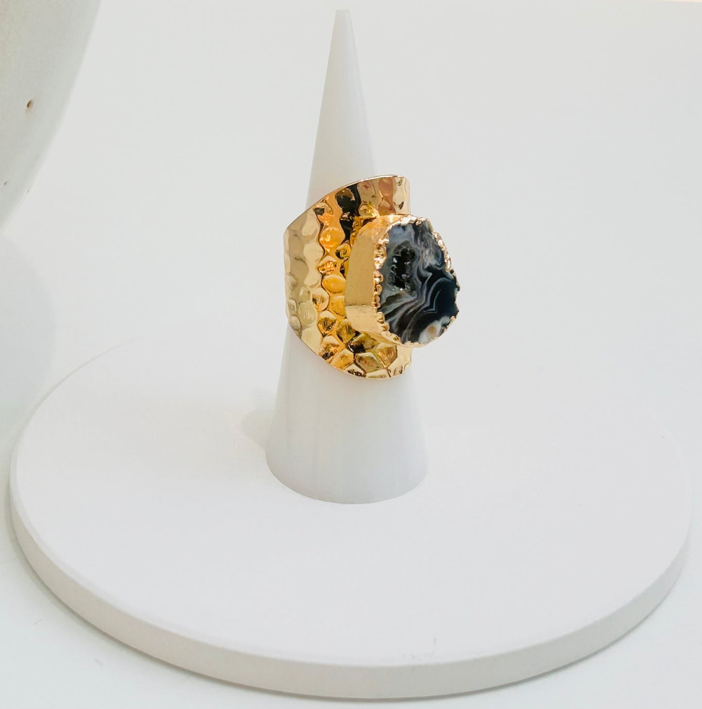 
                  
                    A gold ring with a large black and white marbled geode stone, displayed on a white cone stand against a white background.
                  
                