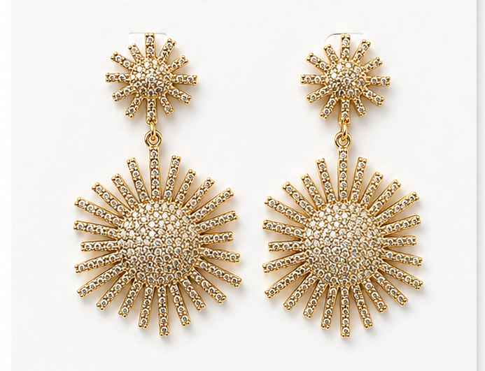 
                  
                    A pair of gold-toned dangle earrings with starburst designs, featuring a smaller sunburst stud at the top and a larger sunburst drop below, both adorned with clear rhinestones on a white background.
                  
                