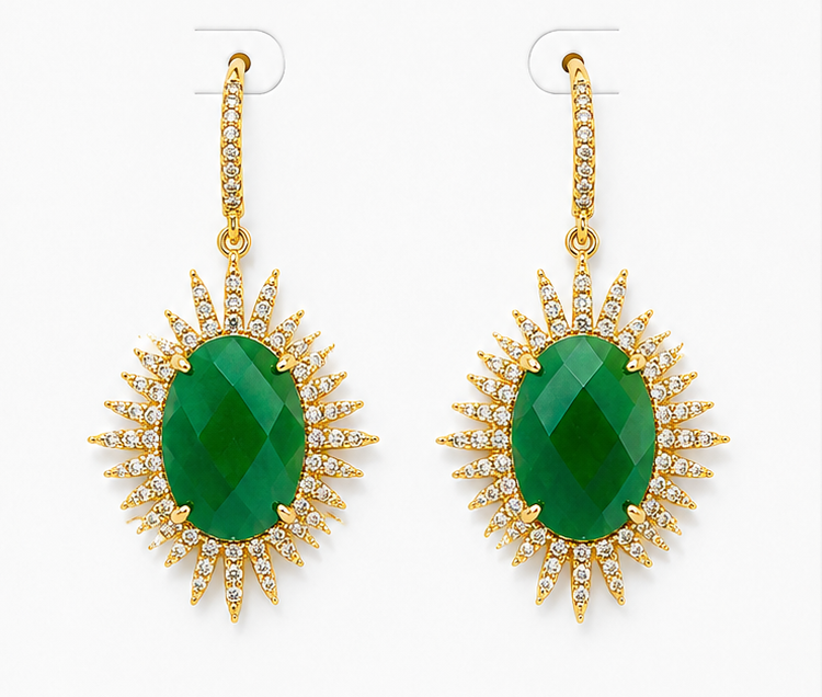 
                  
                    A pair of gold drop earrings featuring oval-cut green gemstones surrounded by a sunburst halo of small clear stones, shown on a plain light background.
                  
                