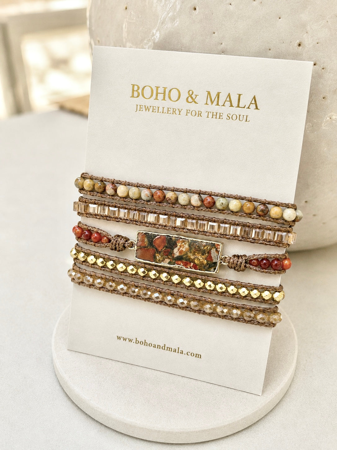 
                  
                    A stack of bohemian-style red jasper mixed beaded bracelets displayed on a white card from BOHO & MALA, set against a soft-focus neutral background.
                  
                
