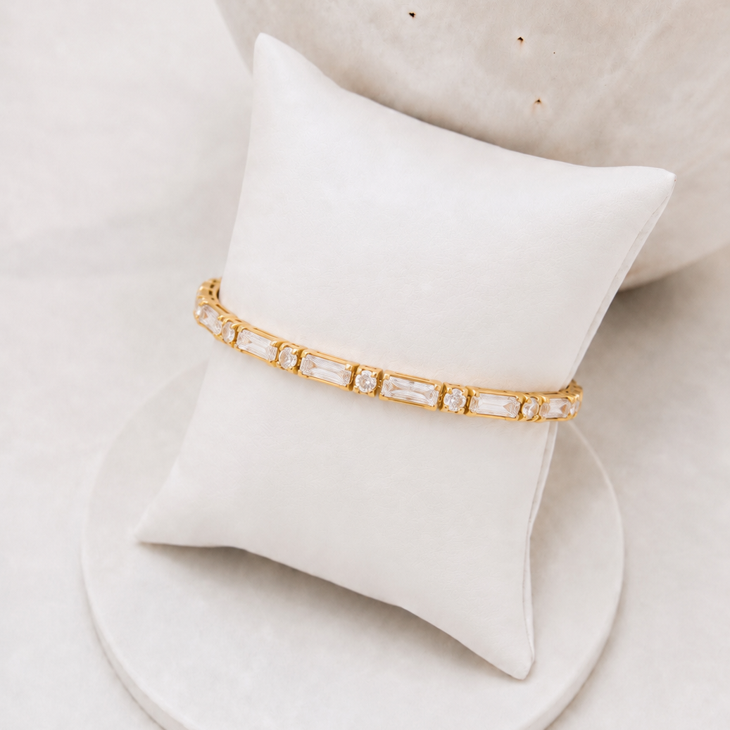 
                  
                    Avelisse Emerald & Round Crystal Gold Tennis Bracelet displayed on a white stand
                  
                