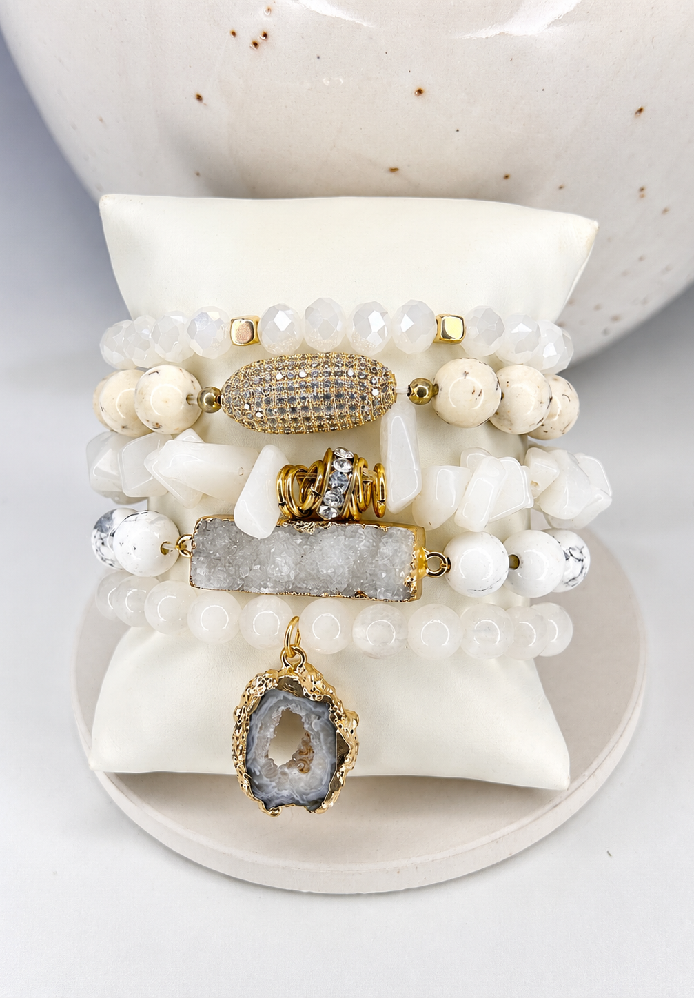 
                  
                    Stack of natural beaded stones bracelets with gold and silver accents on a white surface, including druzy crystals.
                  
                