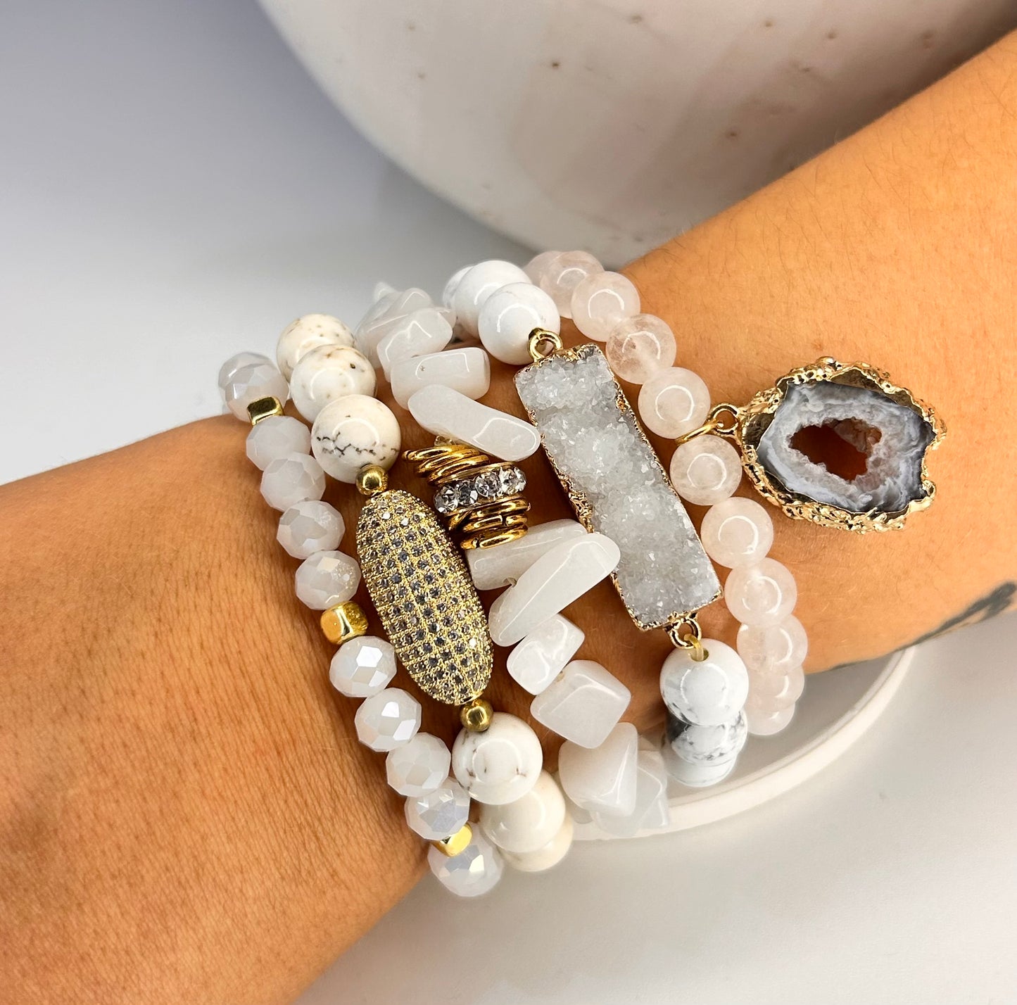 
                  
                    Stack of beaded  natural stone bracelets with acents of druzy and gold accents on a wrist.
                  
                