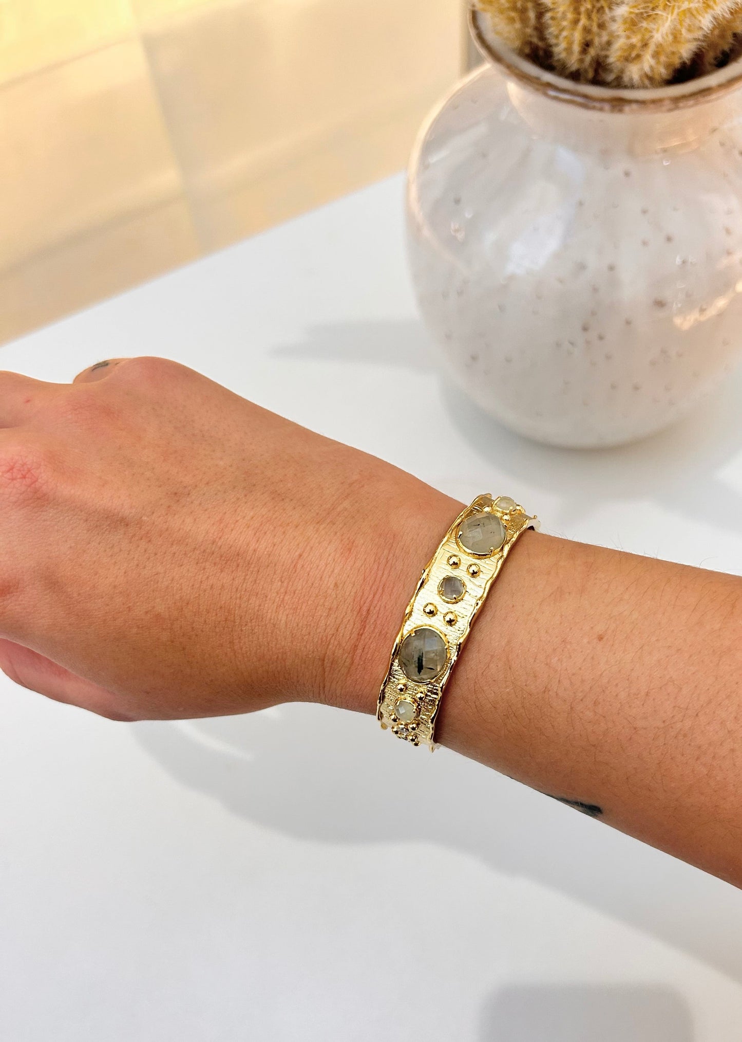 
                  
                    Gold-plated open cuff bracelet featuring natural prehnite gemstones and delicate crystal accents, on model wrist 
                  
                