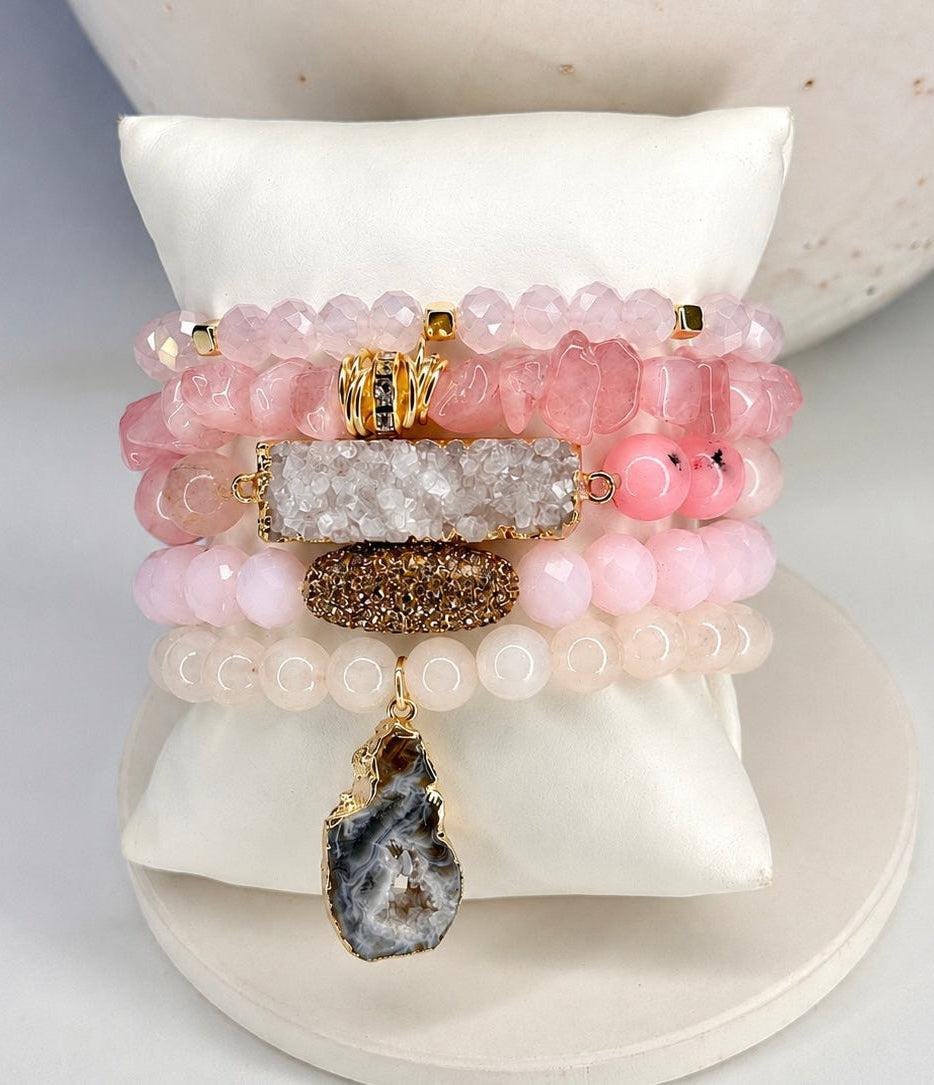 
                  
                    Stack of pink rose quartz beaded bracelets with natural stone and gold accents on a white surface.
                  
                