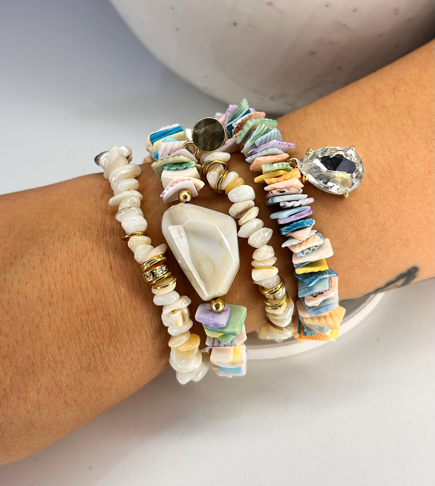 
                  
                    Multicolored shell beaded bracelets on a wrist with a neutral background
                  
                
