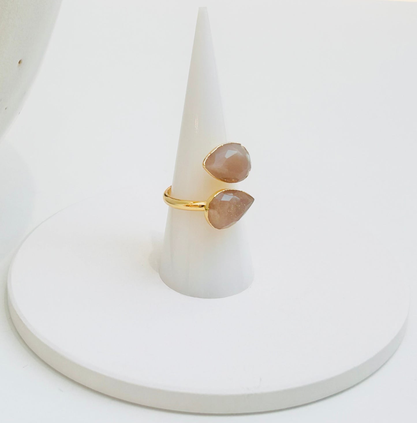 
                  
                    A gold ring with two teardrop-shaped sunstone gemstones, displayed on a white cone ring holder against a white background.
                  
                
