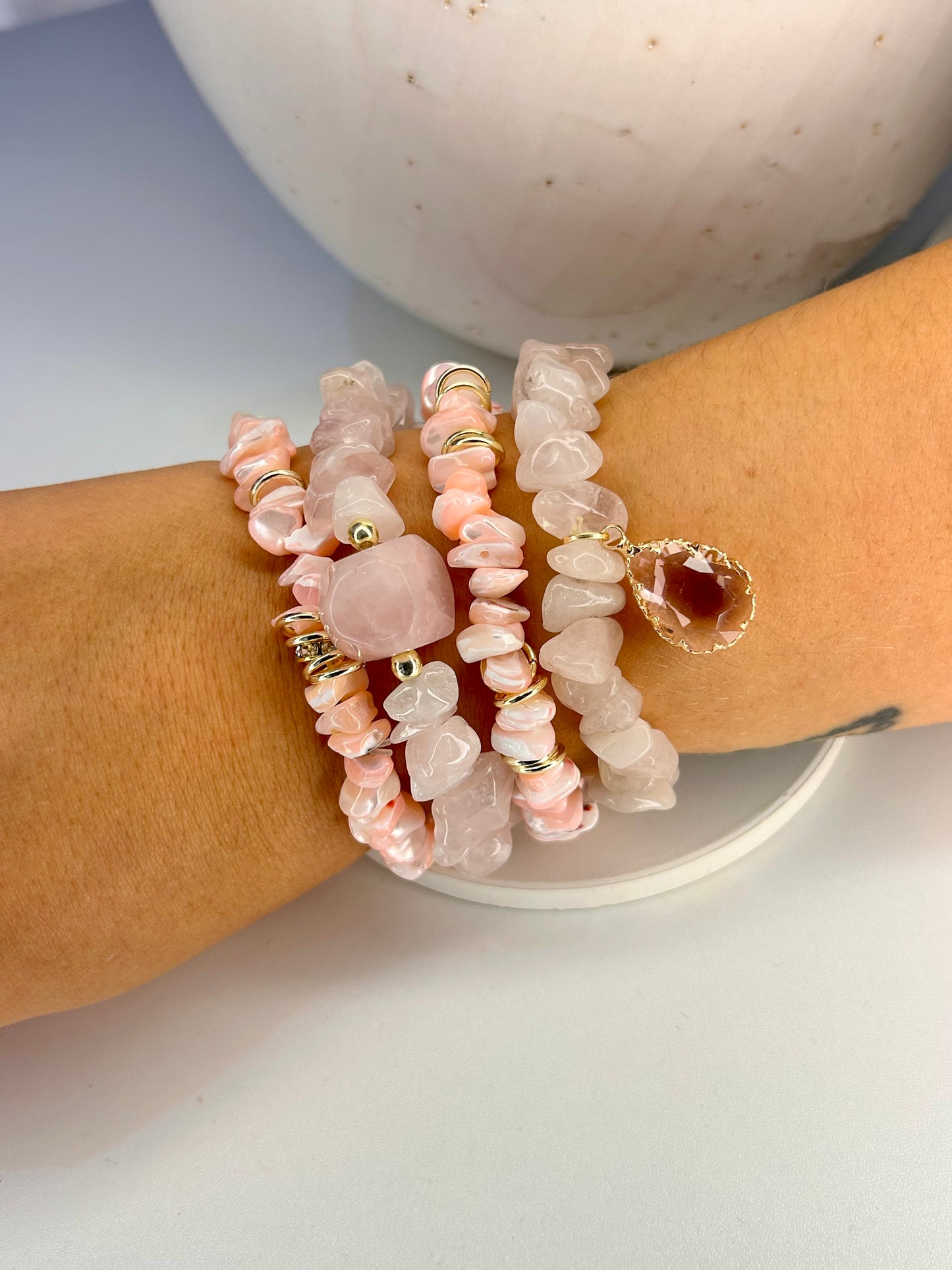 
                  
                    Stack of pink rose quartz beaded bracelets on a wrist with a neutral background
                  
                