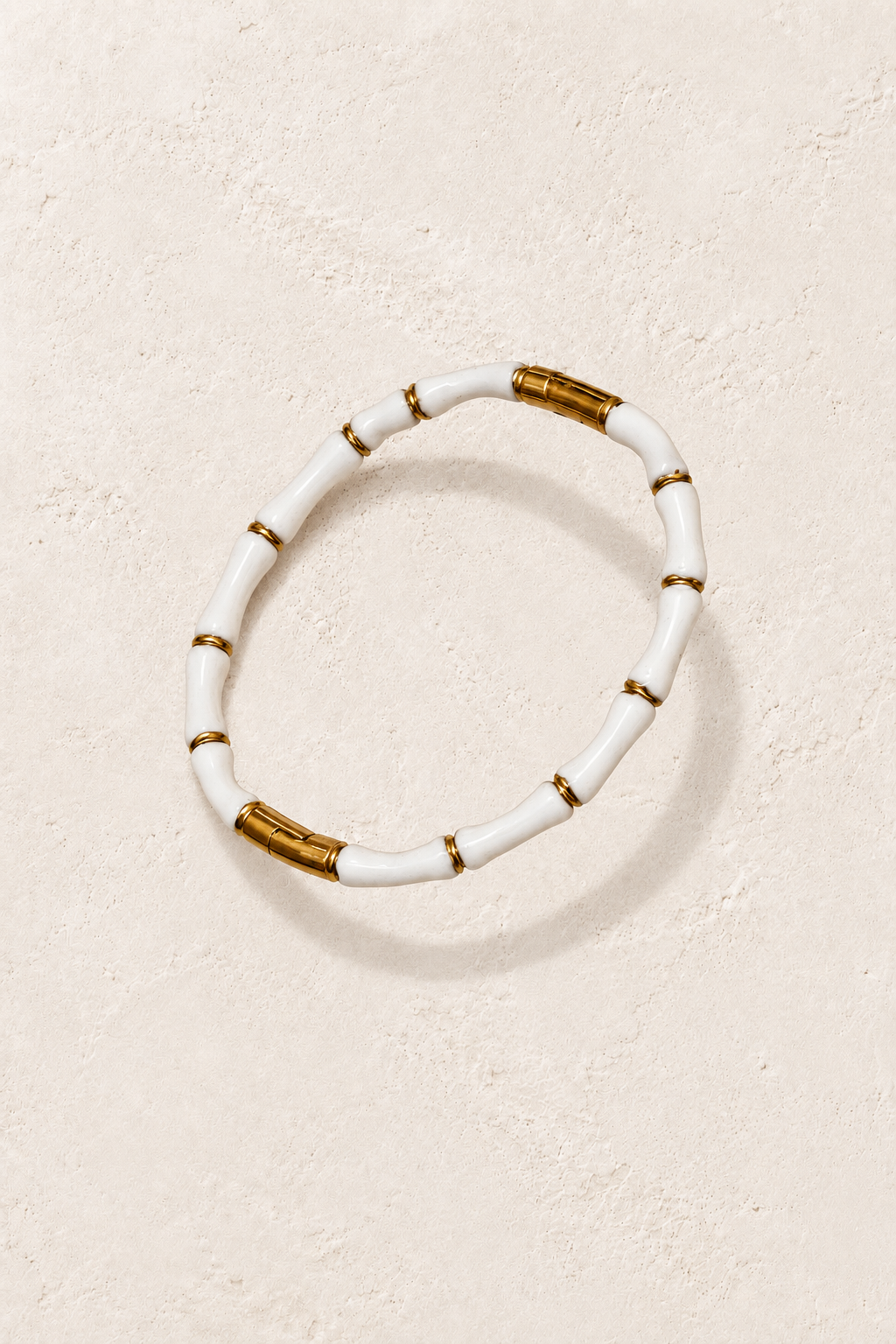 
                  
                    Amaya White Enamel & Gold Bangle on cream beige textured background
                  
                