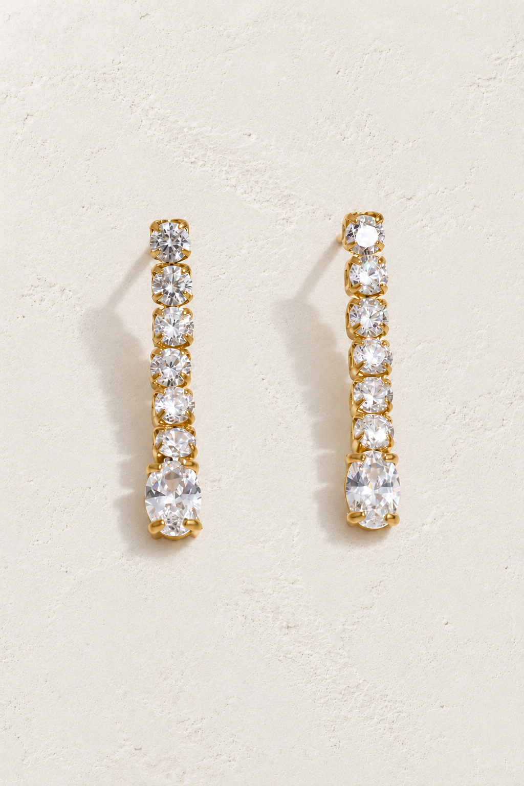 
                  
                    Gold crystal line and oval drop earrings on approved cream hero background
                  
                