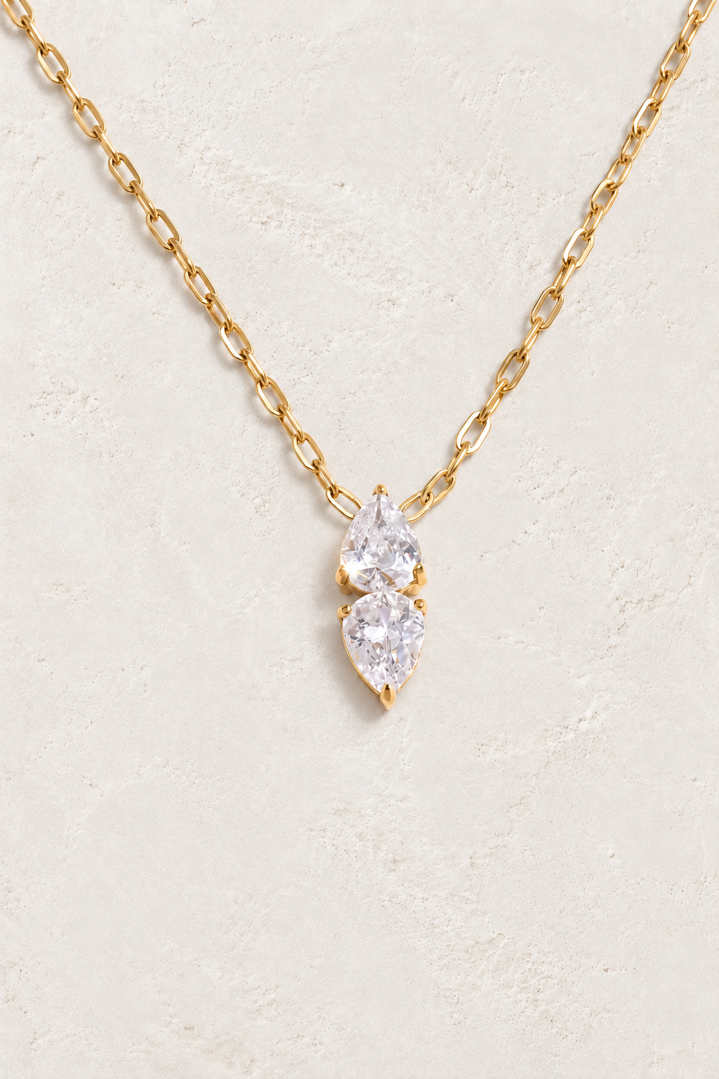 
                  
                    Gold double teardrop cubic zirconia necklace on approved cream hero background
                  
                
