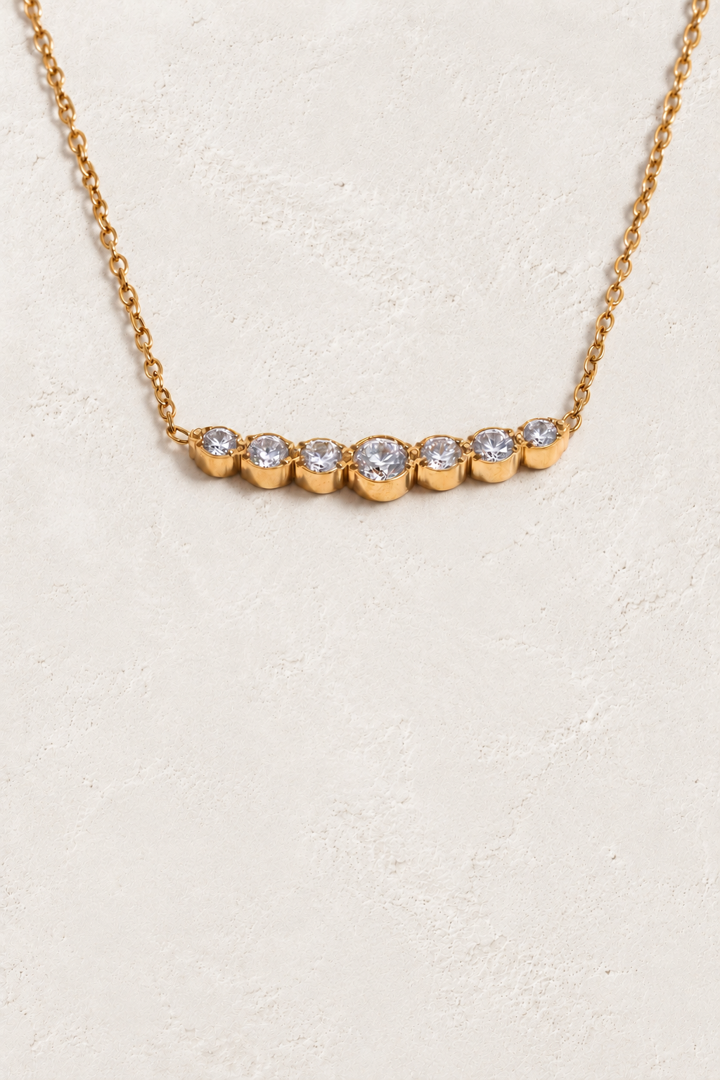 
                  
                    Gold seven-stone cubic zirconia necklace on approved cream hero background
                  
                