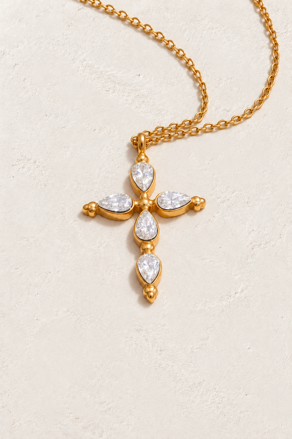 
                  
                    Gold teardrop cross necklace on approved cream hero background
                  
                