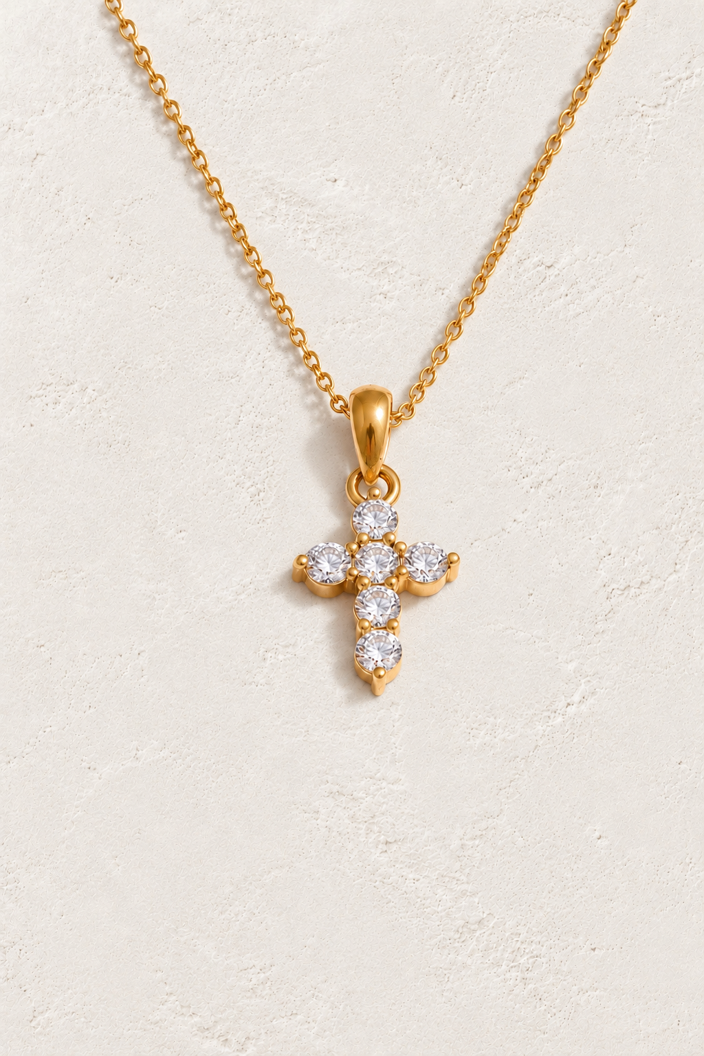 
                  
                    Gold petite six stone cross necklace on approved cream hero background
                  
                