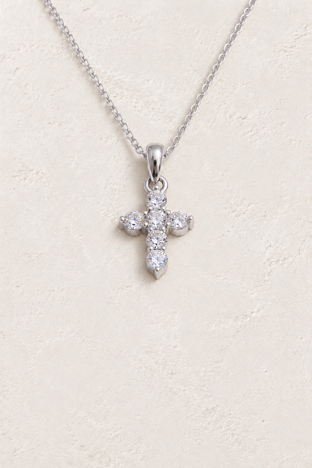 
                  
                    Silver petite six stone cross necklace on approved cream hero background
                  
                