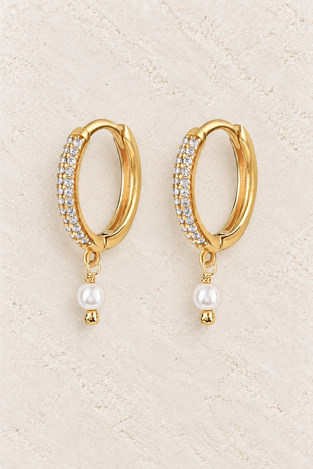 Arielle Pearl & CZ Huggie Earrings on warm cream textured background