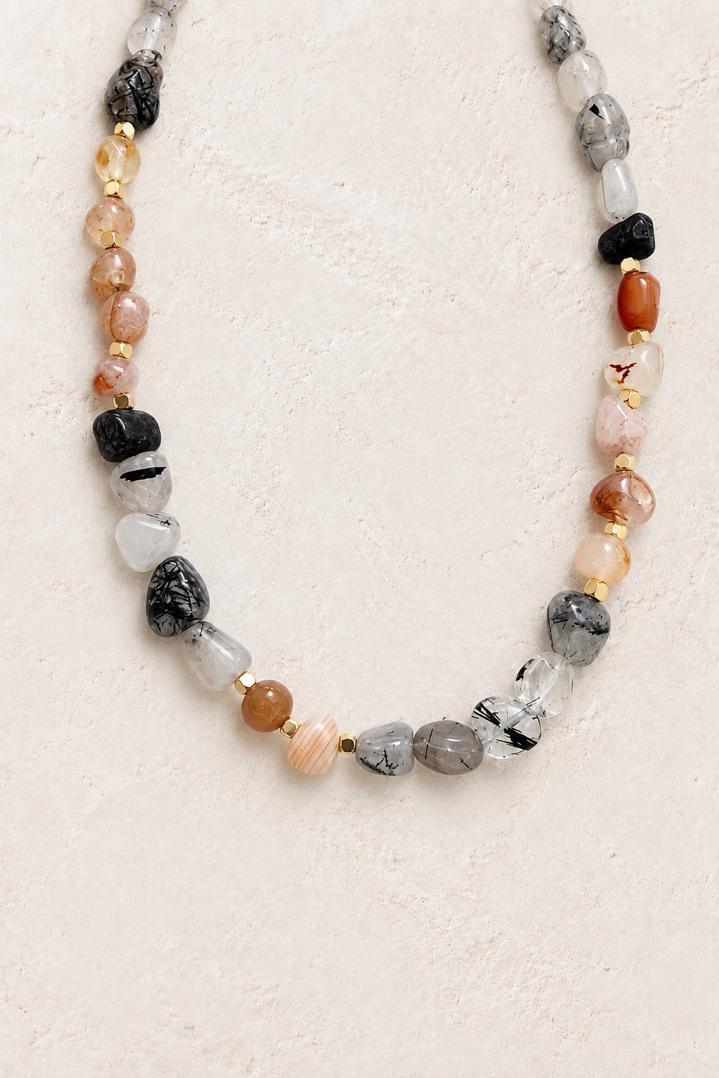 
                  
                    Arvela mixed gemstone necklace with organic stones and gold spacers on a neutral background
                  
                