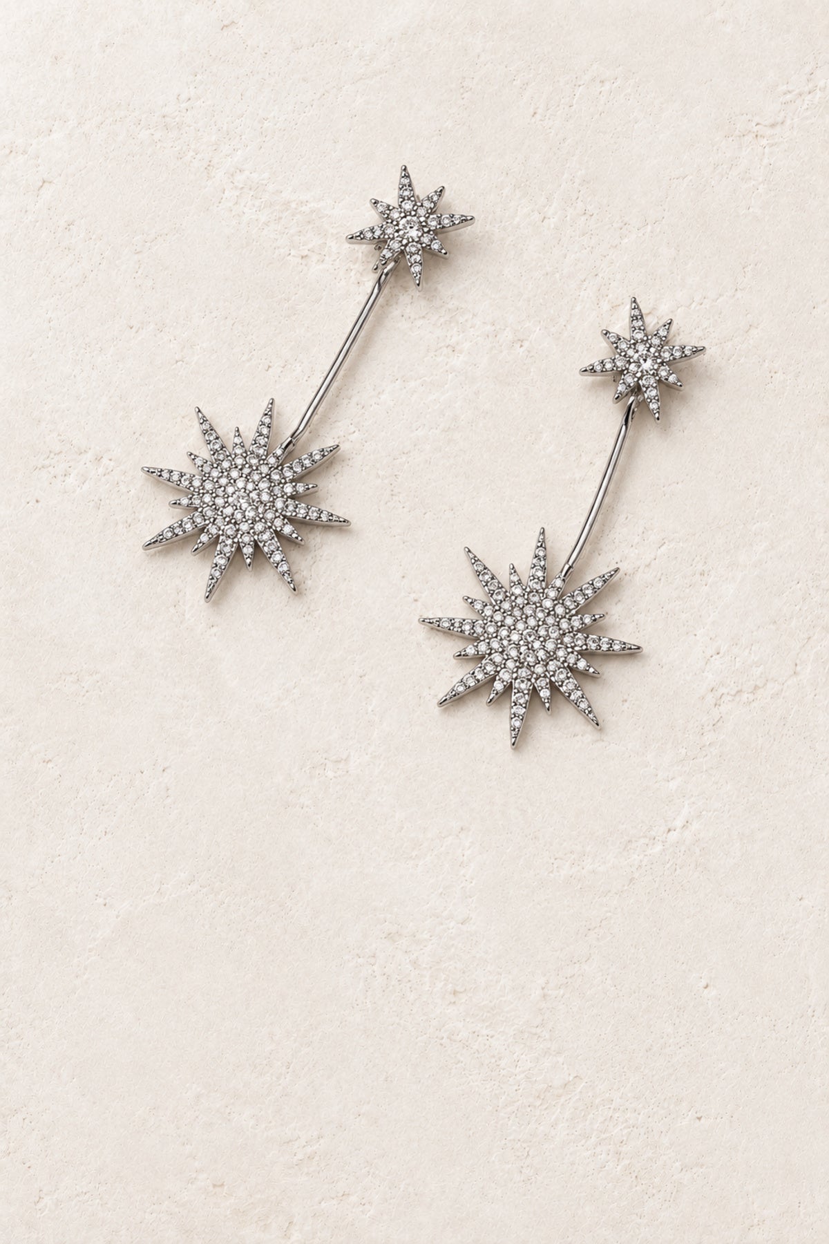 
                  
                    Asteria Silver Starburst Drop Earrings on warm ivory plaster
                  
                