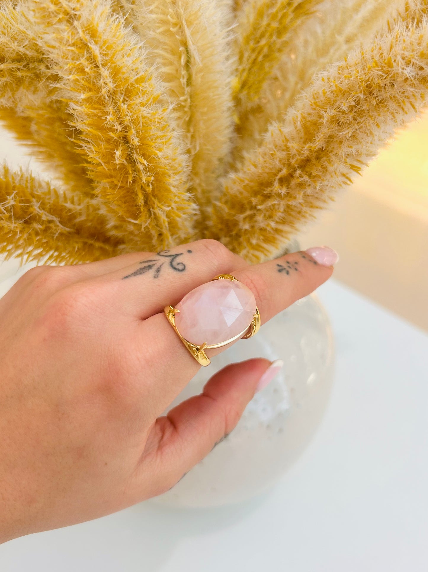 
                  
                    Aurevia Rose Quartz Statement Ring featuring a natural blush-pink oval gemstone set in a sculptural tarnish-free gold-plated band. Worn on models wrist 
                  
                
