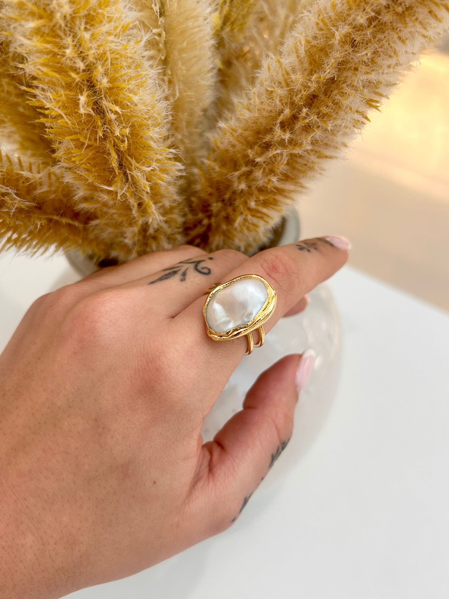 
                  
                    Hand wearing the Avenelle Freshwater Pearl Statement Ring featuring a large organic oval pearl in a delicate double-band gold-plated design.
                  
                