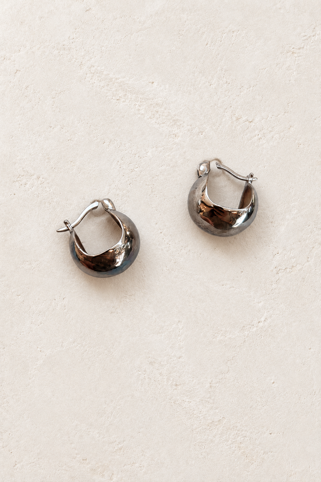 
                  
                    Aviana silver crescent hoop earrings on warm ivory plaster
                  
                