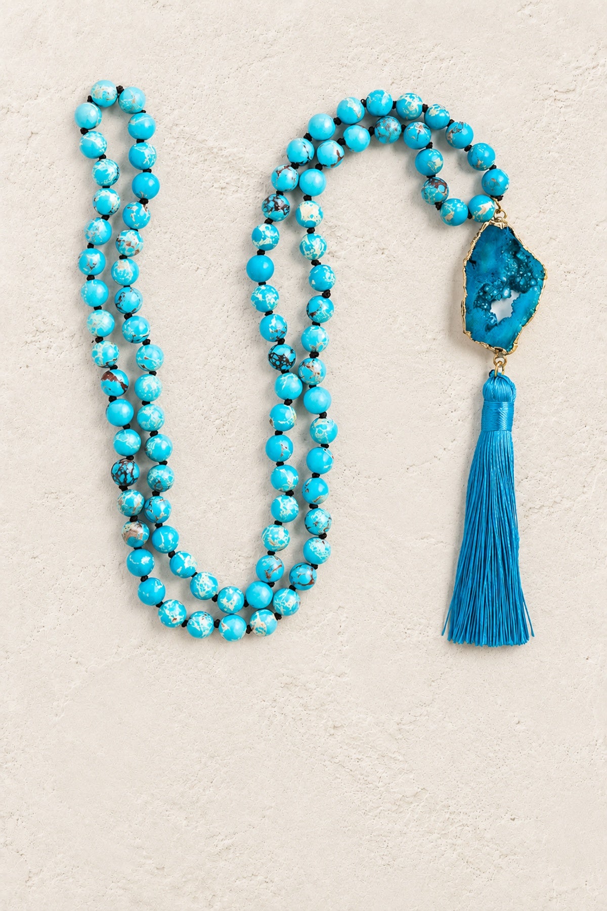 
                  
                    Blue Agate Slice Tassel Necklace on warm cream plaster background
                  
                