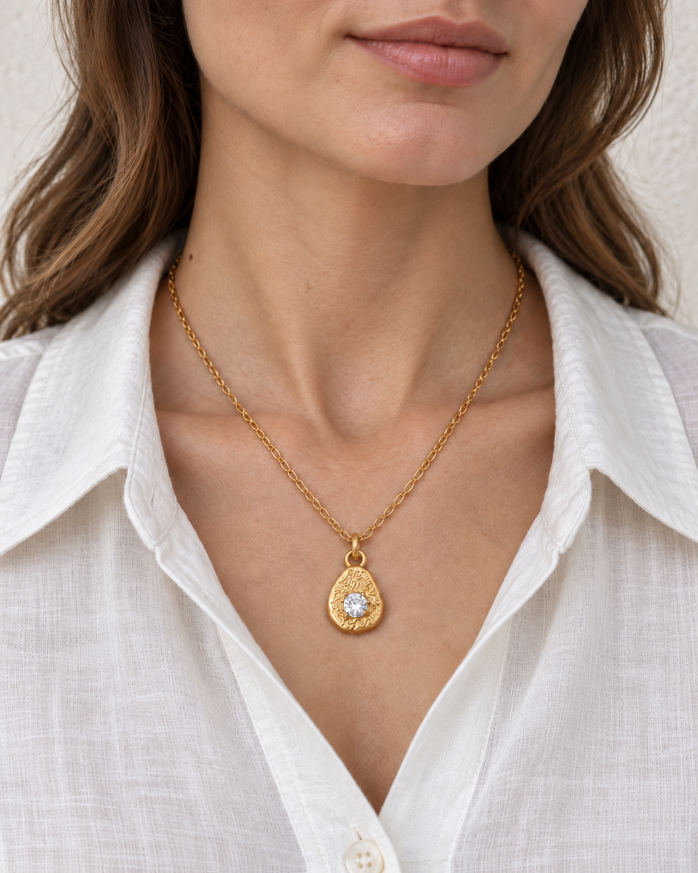 A model wearing Boho &amp; Mala's Aurelia Crystal Pendant Necklace with an ivory V-neck shirt.