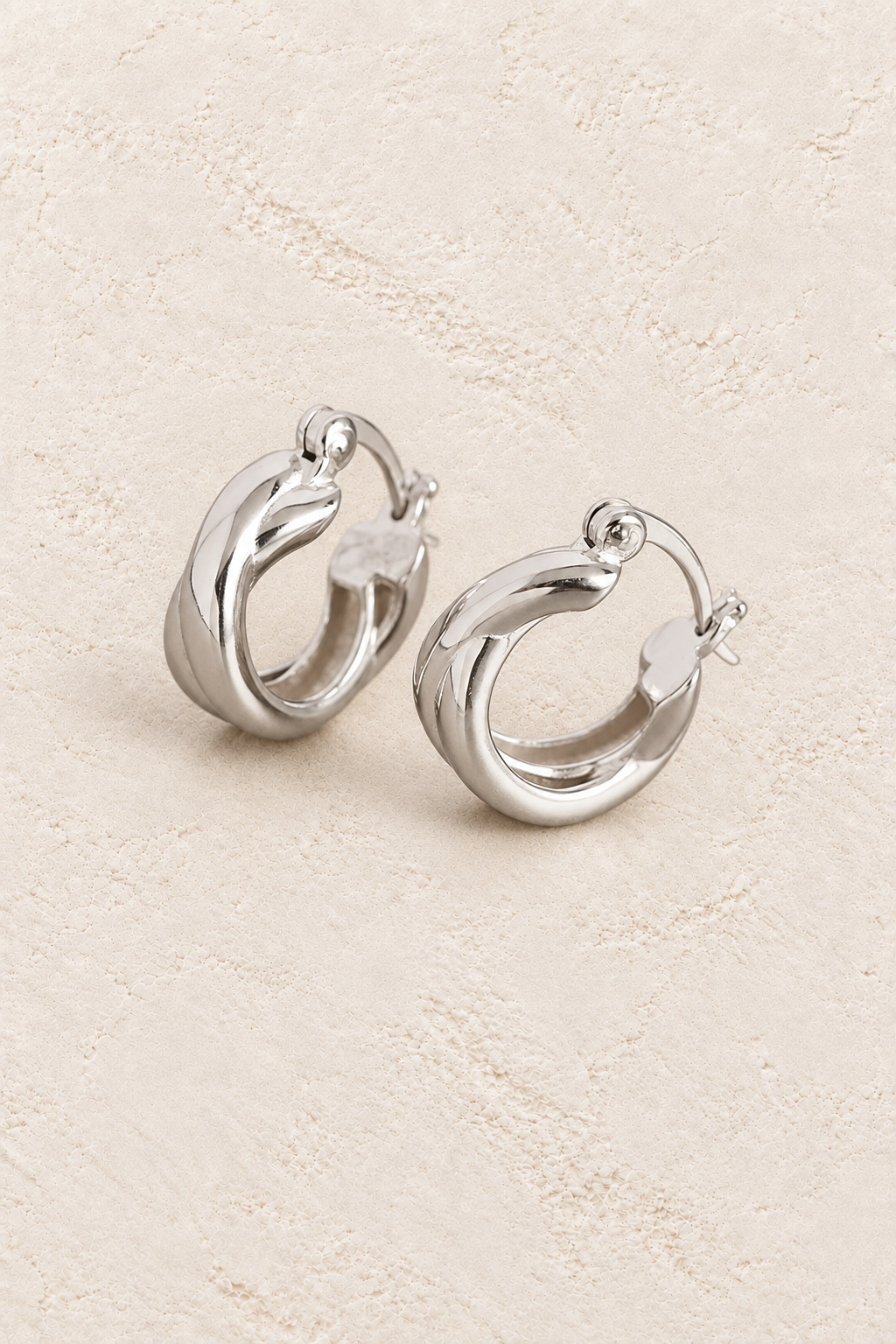 
                  
                    Boho & Mala Sterling Silver Hoop Huggie Earrings on warm cream textured background
                  
                