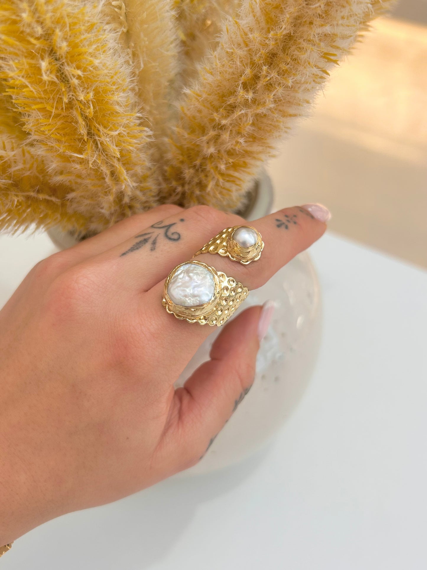 
                  
                    Hand wearing the Calista Freshwater Pearl Statement Ring featuring one large organic pearl and a smaller pearl in an adjustable gold-plated design.
                  
                