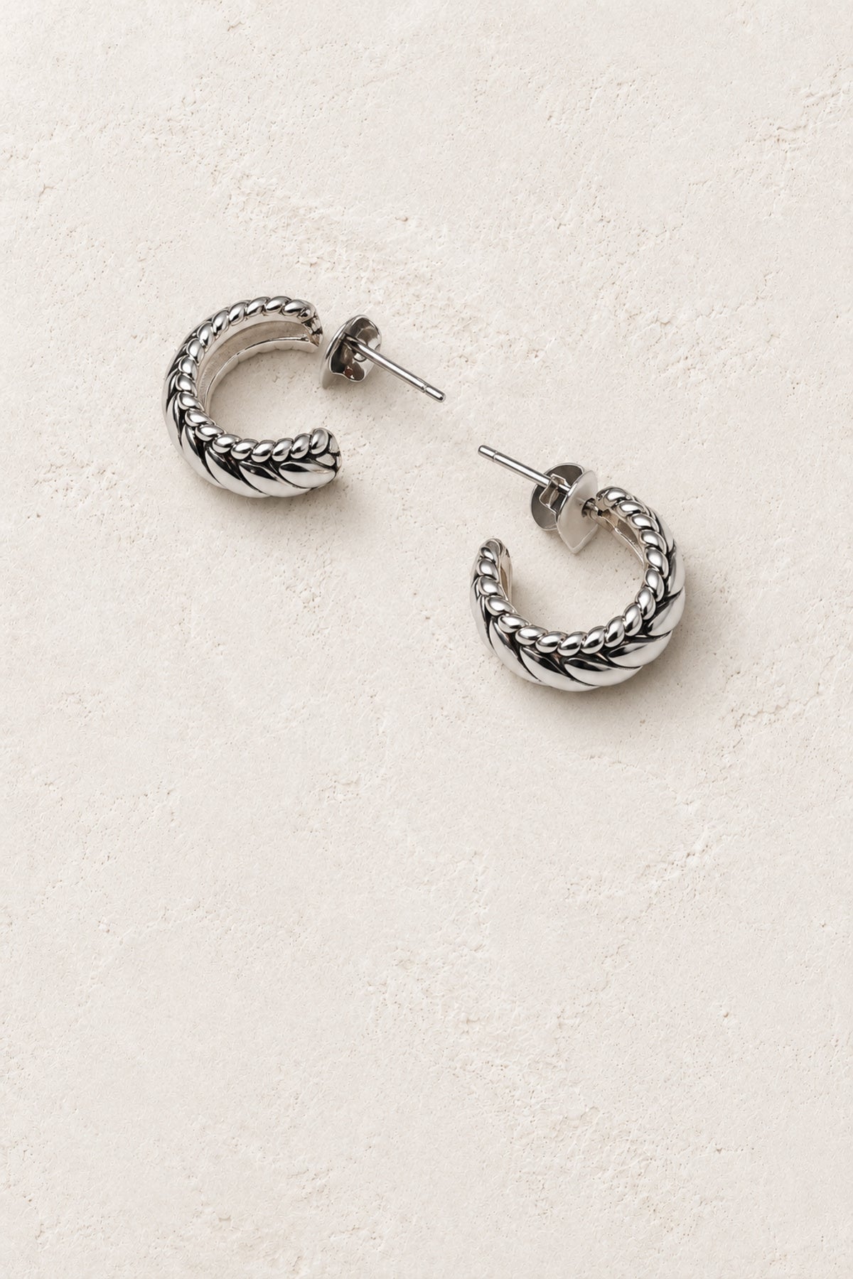 
                  
                    Callista Silver Braided Mini Hoop Earrings on warm ivory plaster
                  
                