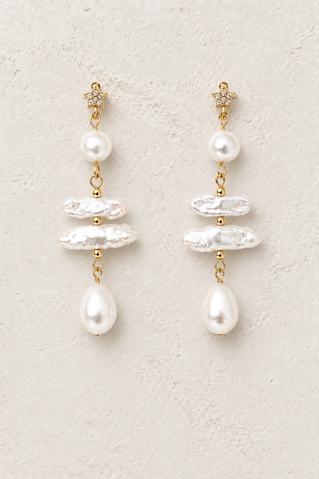 
                  
                    Celestial freshwater pearl star gold drop earrings on warm textured background
                  
                