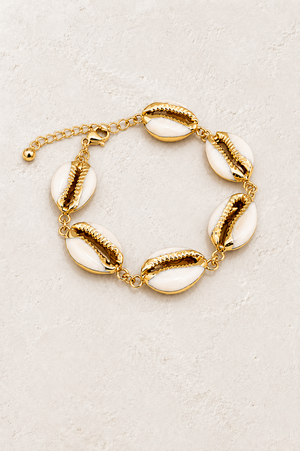 Coastal Muse gold cowrie shell bracelet on a warm off-white textured plaster background