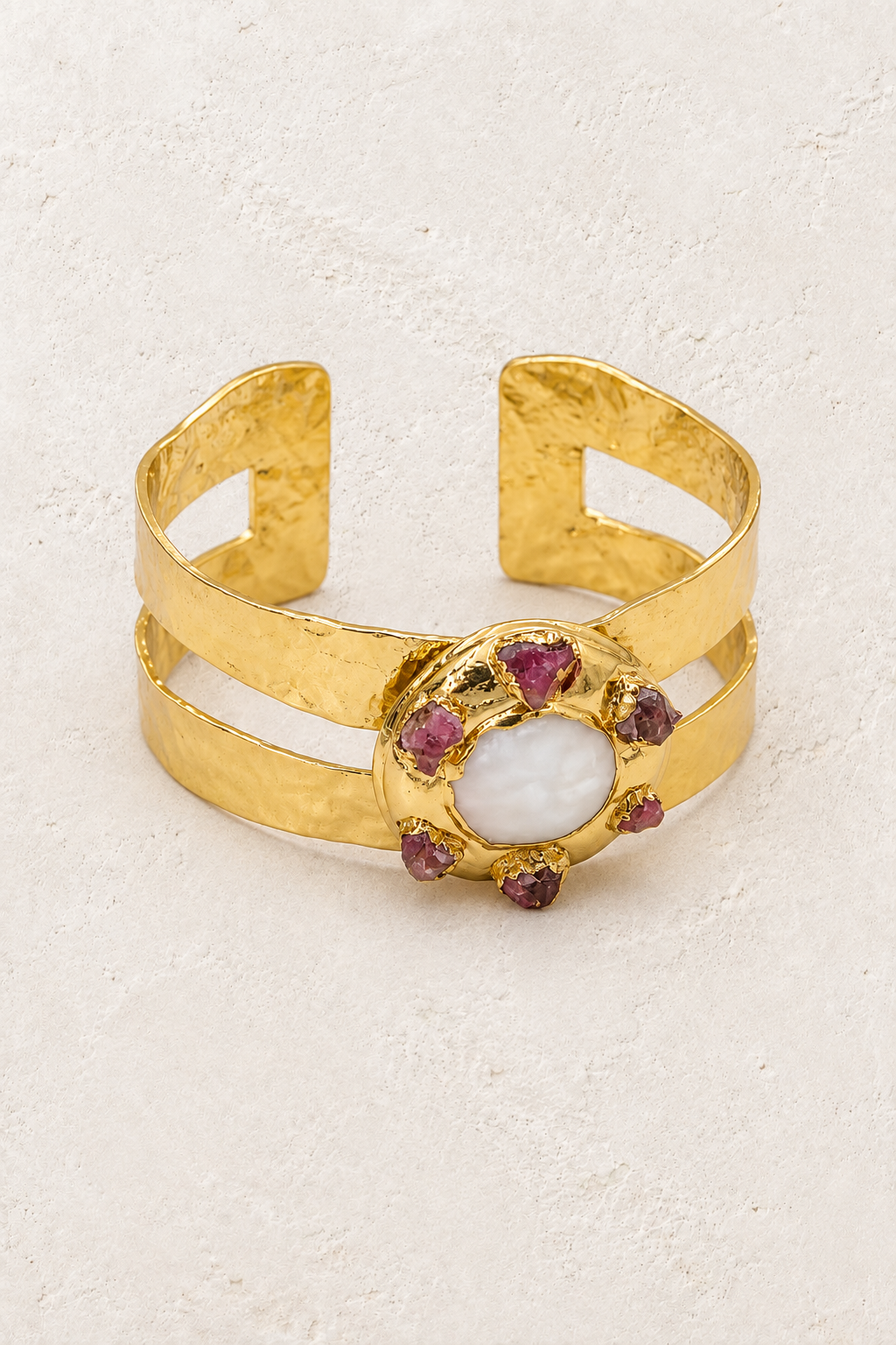Coralia gold pearl and purple stone cuff on a warm off-white textured plaster background