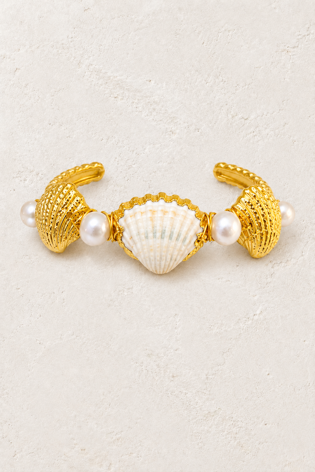Coralia gold shell and freshwater pearl cuff on a warm off-white textured plaster background