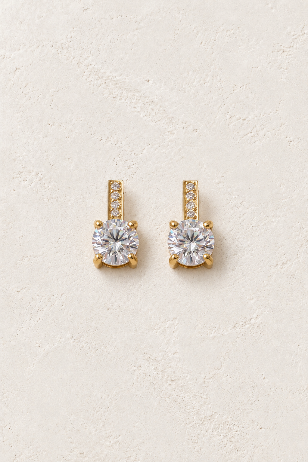 
                  
                    Gold crystal bar solitaire stud earrings on ivory plaster
                  
                
