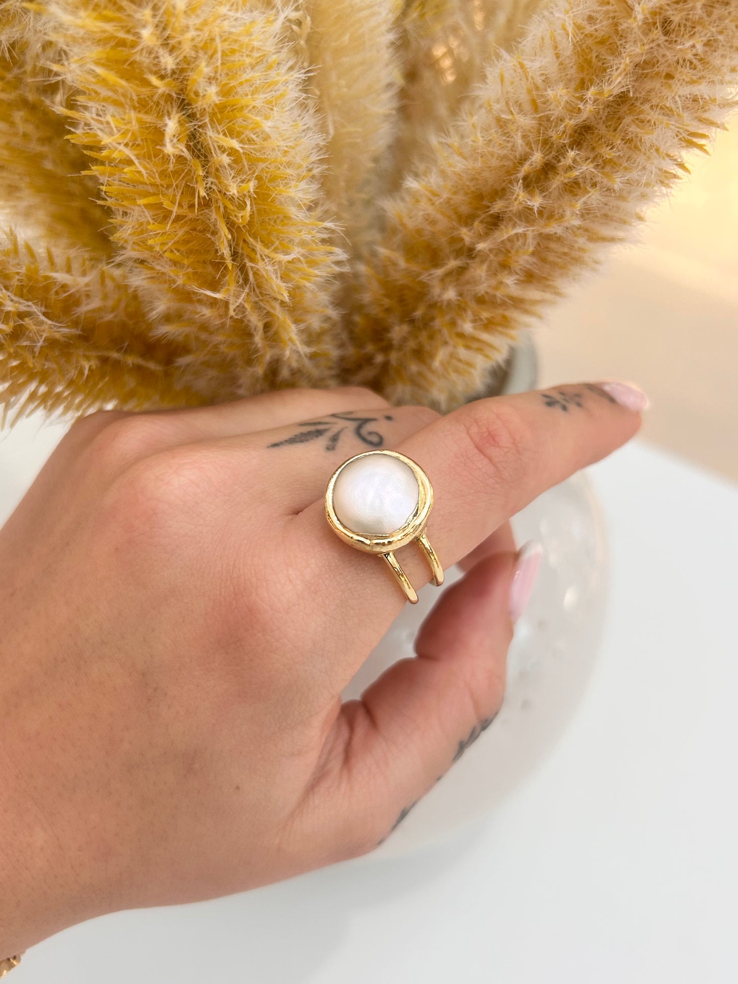 
                  
                    Hand wearing the Elara Freshwater Pearl Statement Ring featuring a smooth round pearl and an adjustable gold-plated double band.
                  
                