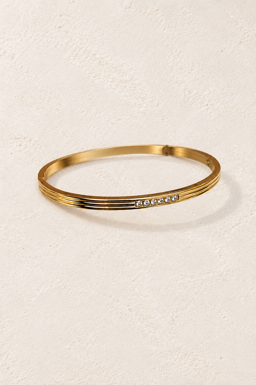 
                  
                    Elira Mini Gold Triple Line Crystal Bangle on cream beige textured background
                  
                