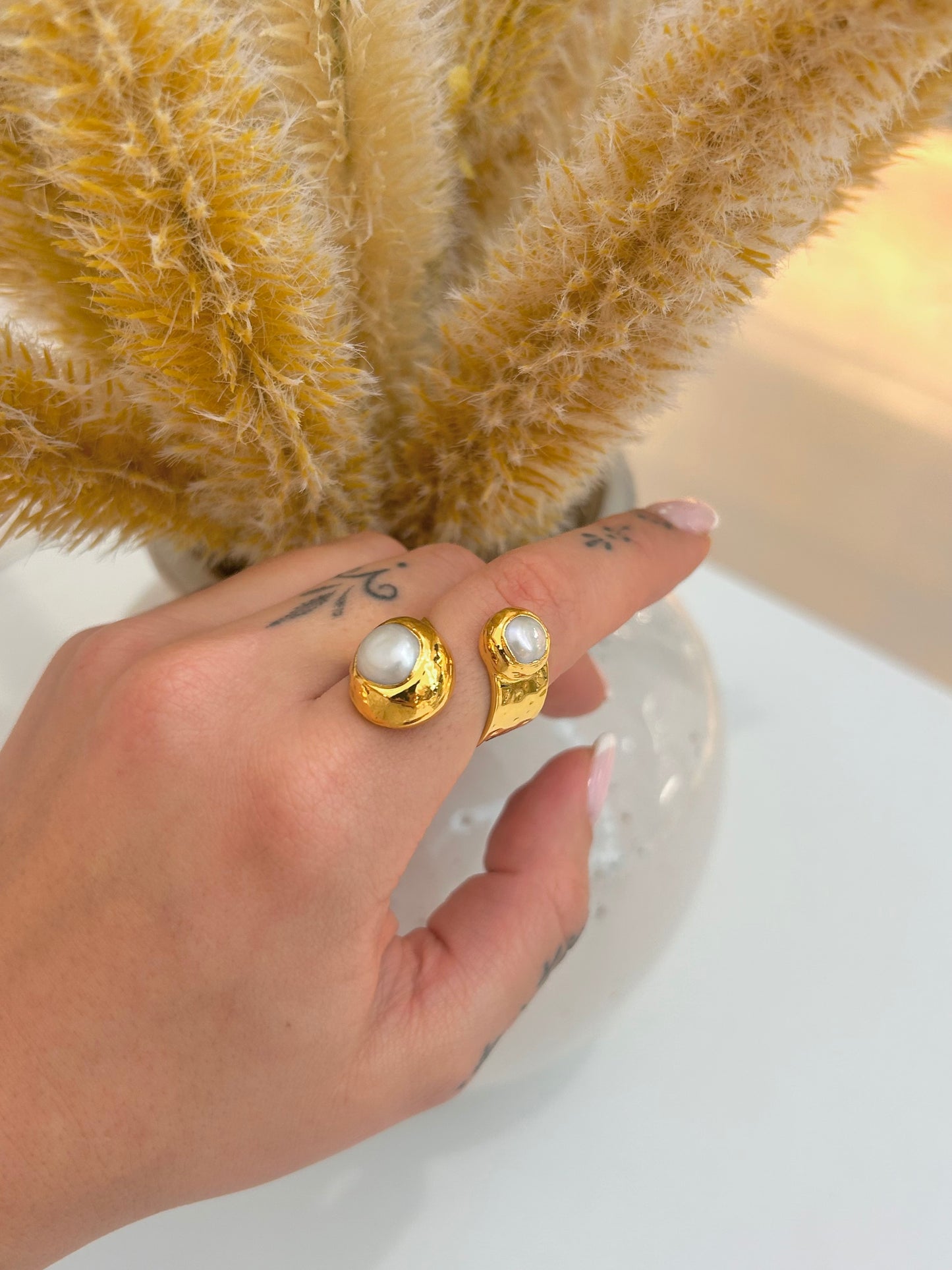 
                  
                    Hand wearing the Elowara Freshwater Pearl Statement Ring featuring two natural pearls and an adjustable open gold-plated band.
                  
                