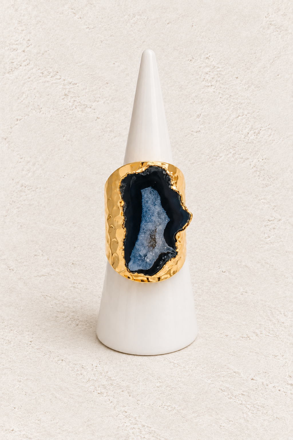 Elowyn Black & Blue Agate Geode Ring on white cone against warm textured background